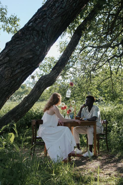 Free A serene romantic outdoor picnic with a couple sitting under a tree enjoying a sunny day. Stock Photo