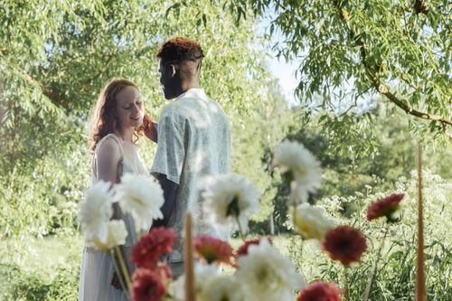 Free A romantic moment between an interracial couple surrounded by vibrant garden flowers. Stock Photo