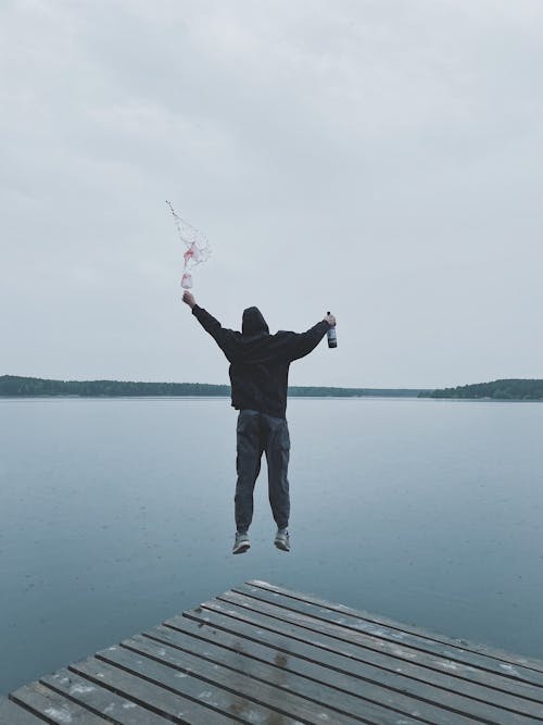 Man Holding Wine Bottle While Jumping from Wooden Dock