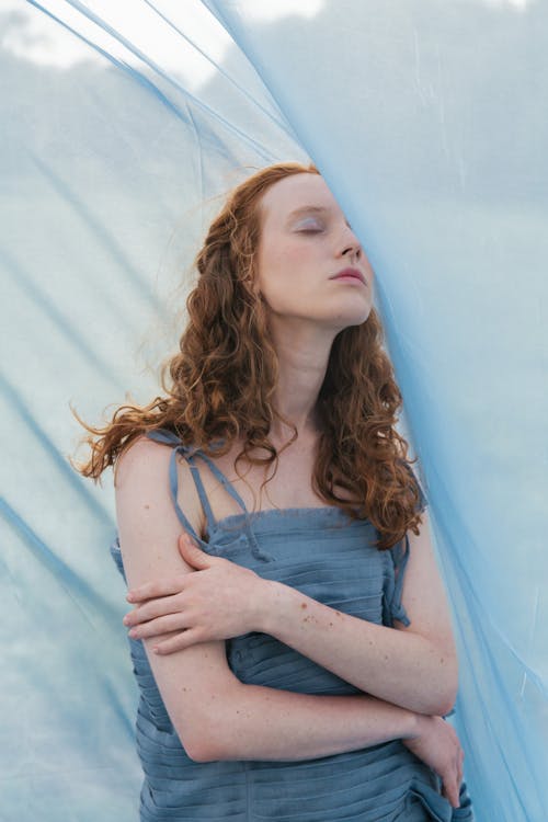 A Woman in Blue Top Beside a Blue Sheer Fabric
