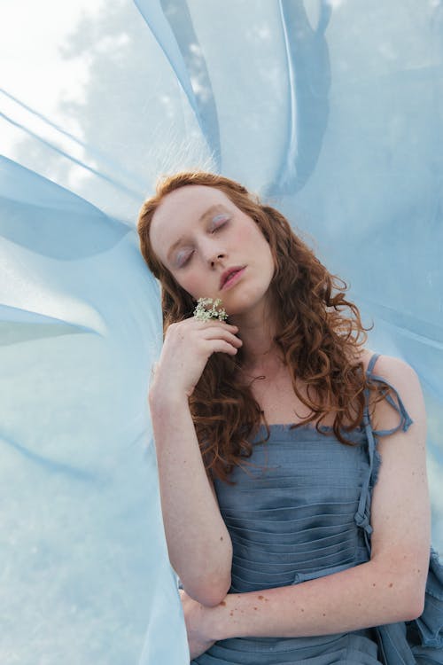 A Woman in Blue Top Beside a Blue Sheer Fabric Holding Tiny Flowers
