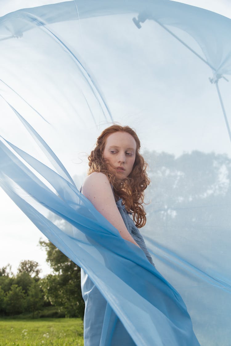 A Woman Standing Beside A Blue Sheer Curtain