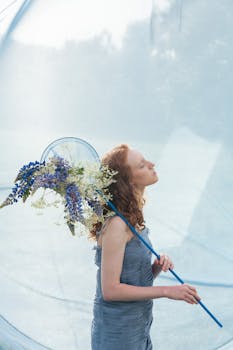 Artistic portrait of a woman holding a flower-decorated net, standing in soft blue tones.