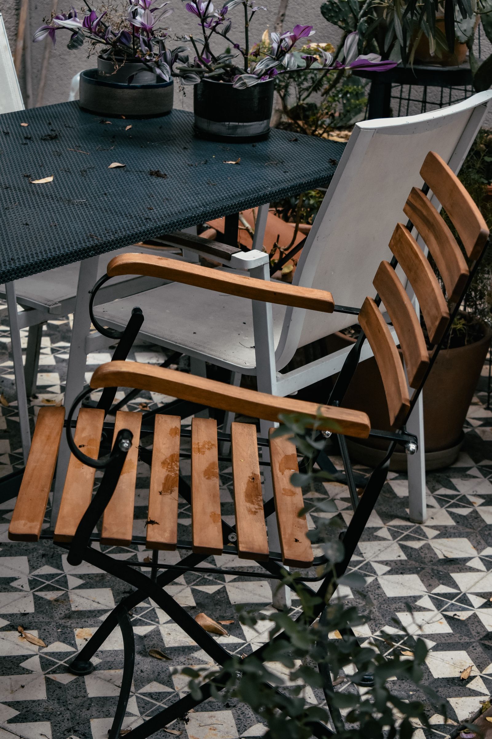 Varanda com cadeiras de madeira, mesa e plantas em vasos.