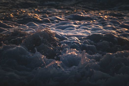 Close-up of ocean waves with sunlit foam during golden hour, showcasing natural beauty.