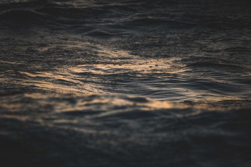 Free Calm waves on the ocean surface reflect a golden sunset, creating a serene atmosphere. Stock Photo