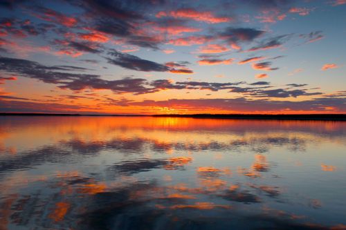 Free A breathtaking sunset painting the sky with vibrant colors over a calm water body, reflecting nature's serene beauty. Stock Photo