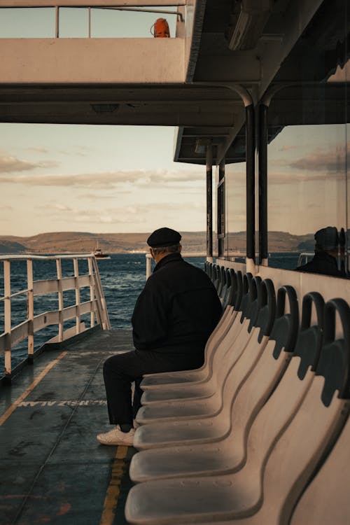 A Man in Black Jacket Sitting on the Seat at the Pier