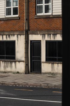 A city building with brick facade, metal door, and barred windows. Quiet street view.