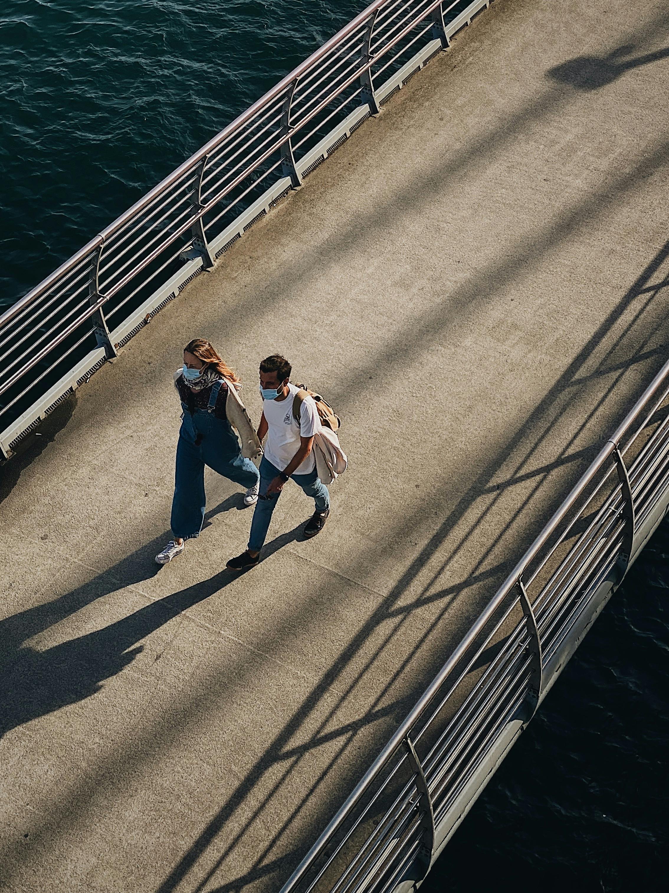 Aerial view of a couple with masks holding hands on a footbridge in Istanbul.