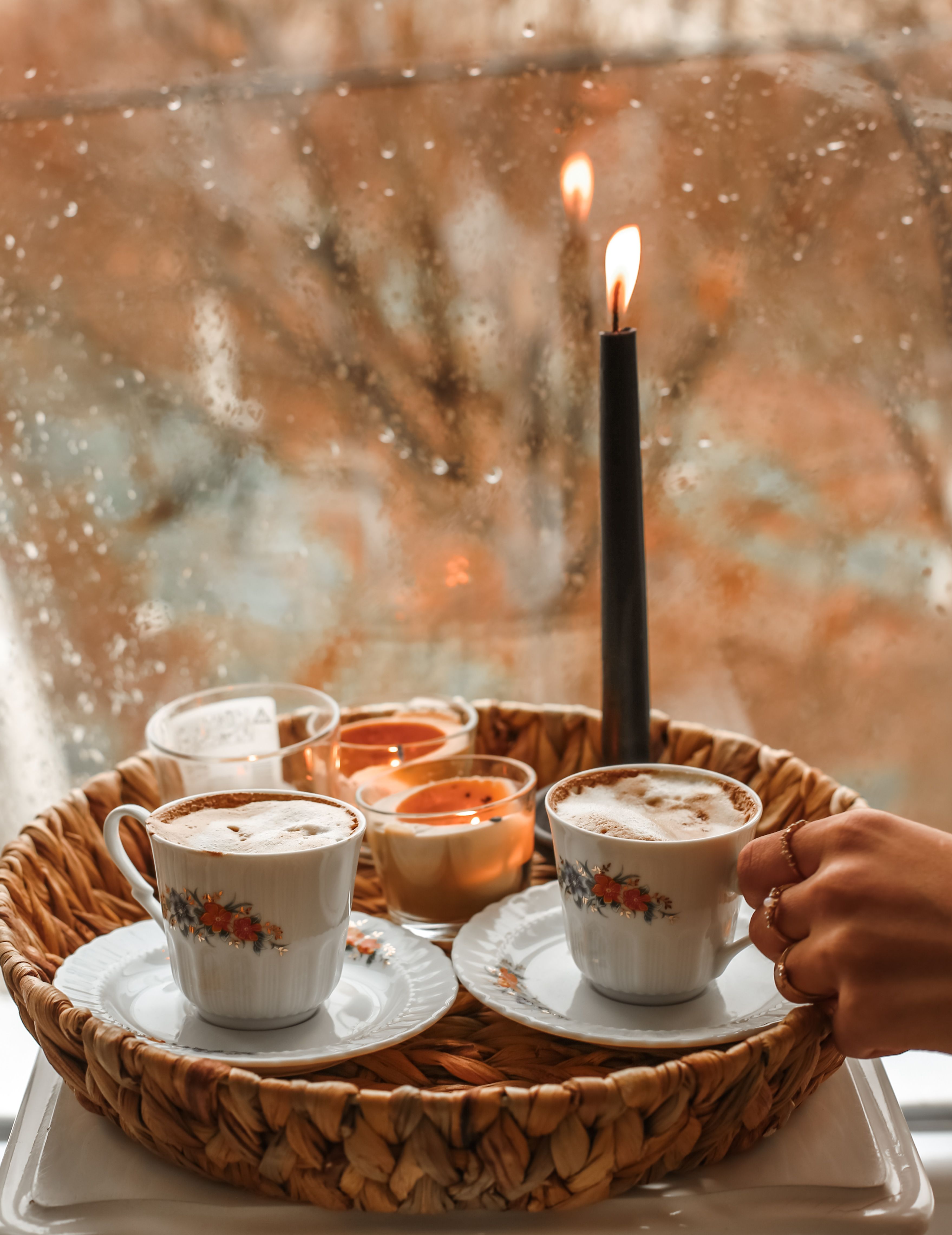 Free Warm autumn setting with coffee cups, candlelight, and a rainy window view creating a cozy atmosphere. Stock Photo