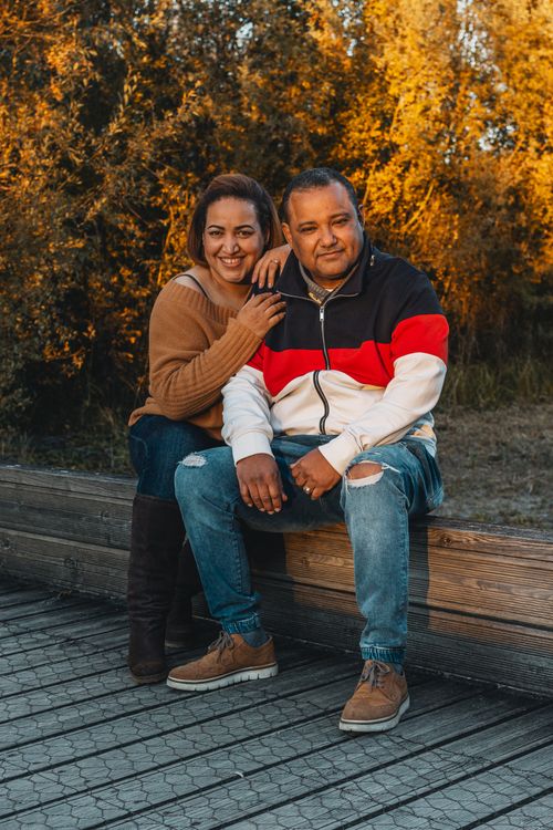 Free Cozy autumn scene with a smiling couple sitting on a wooden bench surrounded by golden foliage. Stock Photo