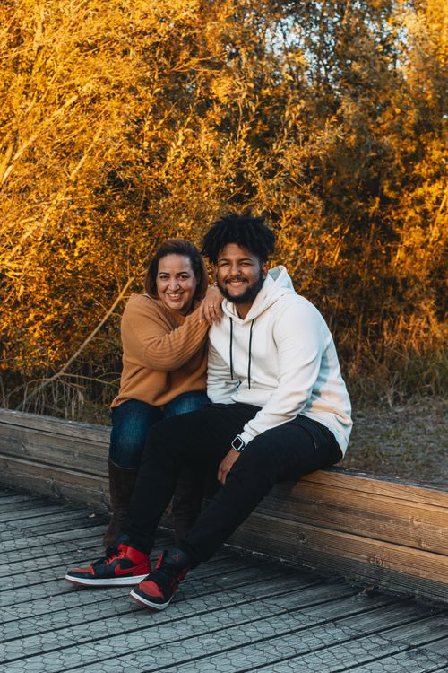 Free Smiling couple sitting together outdoors amidst vibrant autumn foliage. Stock Photo