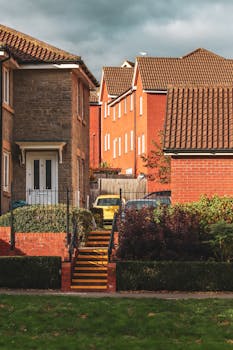 A picturesque suburban scene featuring red brick houses, lawns, and metal stairs under a cloudy sky.
