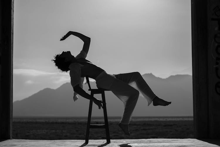 Grayscale Photo Of A Man With Unbuttoned Shirt Dancing On A Bar Stool