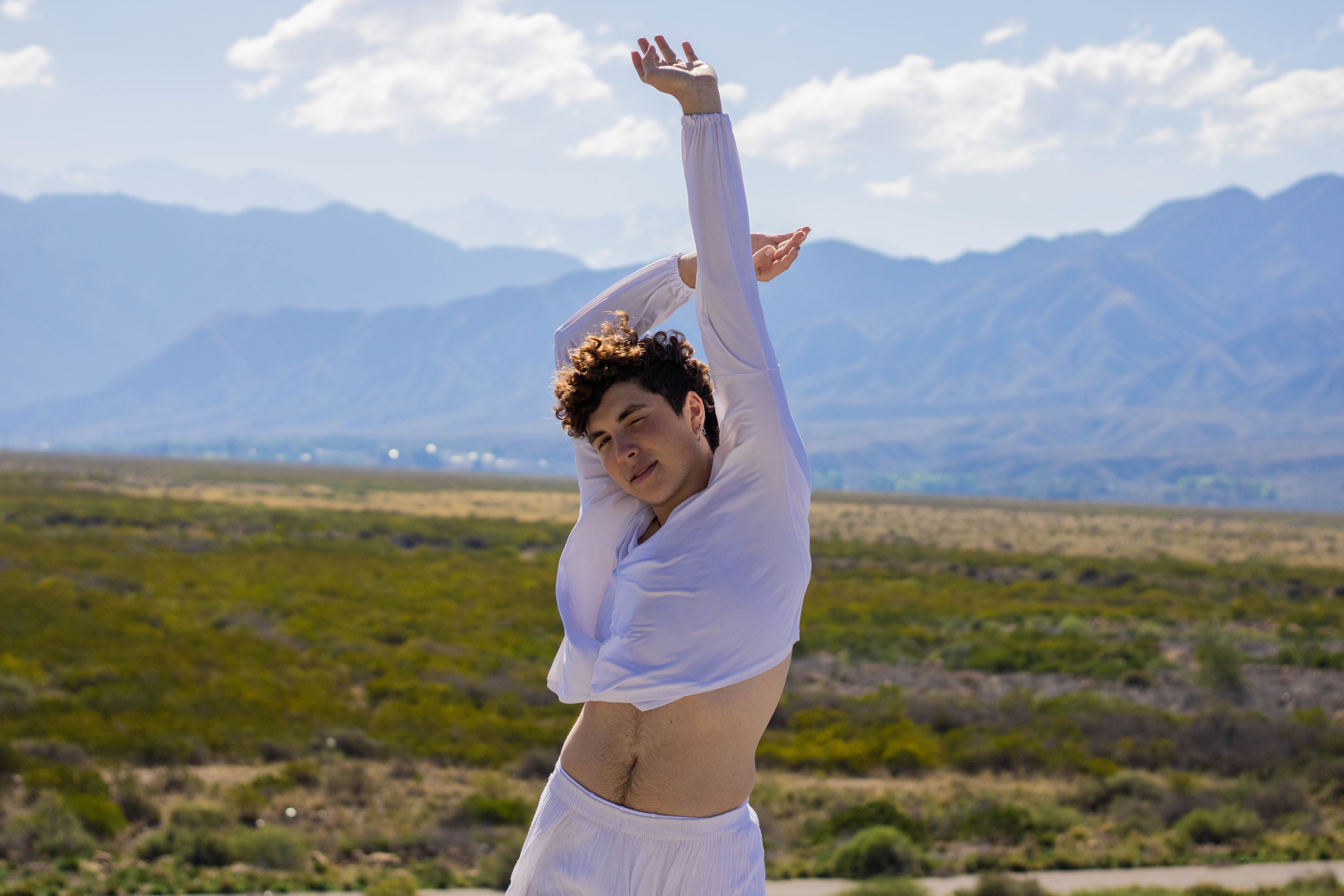 A person doing an open, expansive yoga stretch outdoors with mountains in the background