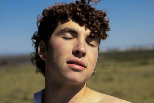 Free Young man with curly hair enjoying the sun with closed eyes. Stock Photo