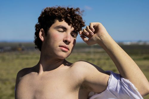 Free A young man confidently poses shirtless against a serene countryside backdrop. Stock Photo