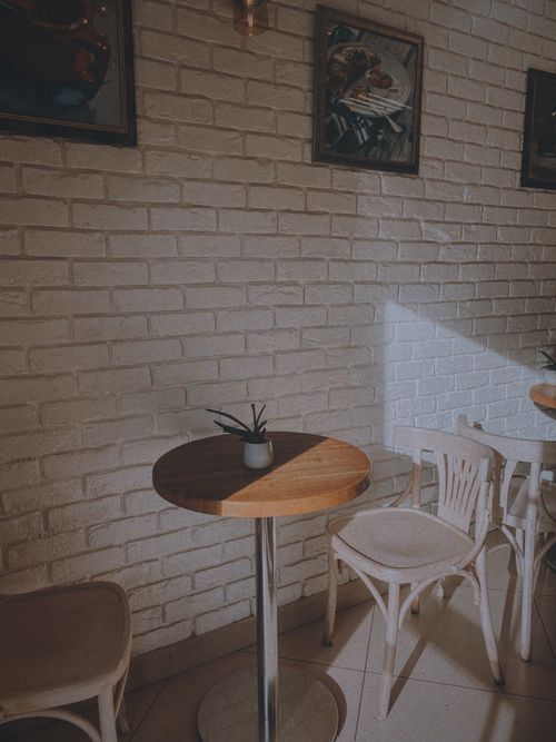 Free Sunlight casts shadows in a cozy cafe corner with brick walls, chairs, and a small plant. Stock Photo