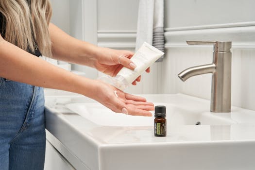 A woman applies lotion next to an essential oil bottle in a modern bathroom.