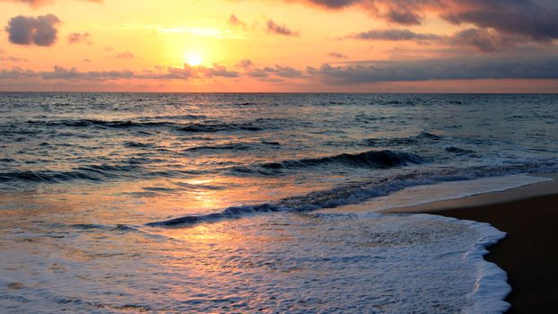 Golden sun setting over a calm ocean with gentle waves hitting a sandy beach.