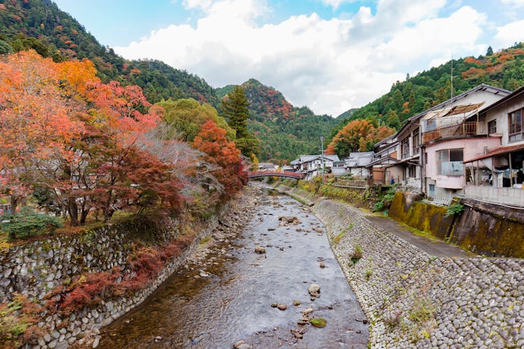 River Flowing Through A Town Surrounded By Forested Hills In Autumn