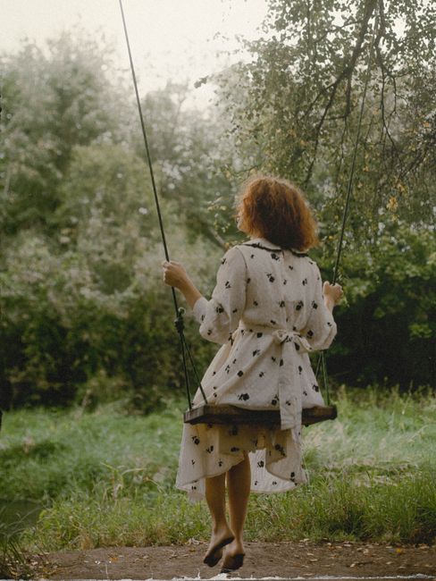 Back view of a woman with curly hair swinging in a lush Moscow park.