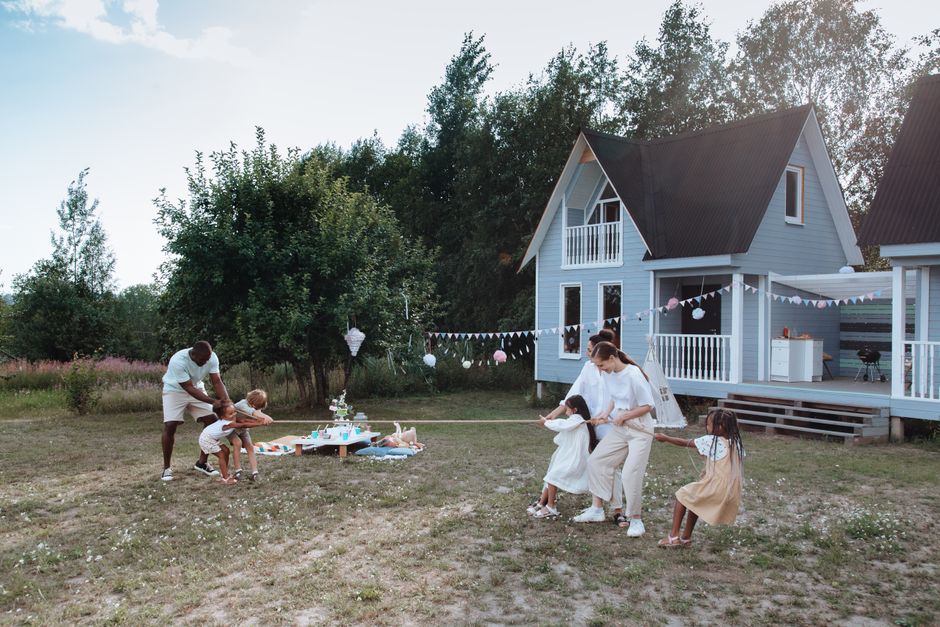 A cheerful family enjoys a tug of war game on a sunny day outside their house, surrounded by nature.