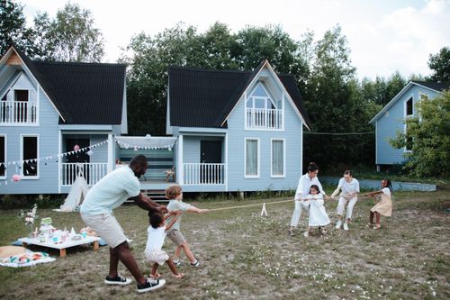 Free A diverse family plays tug of war outdoors near modern houses, enjoying a sunny day. Stock Photo