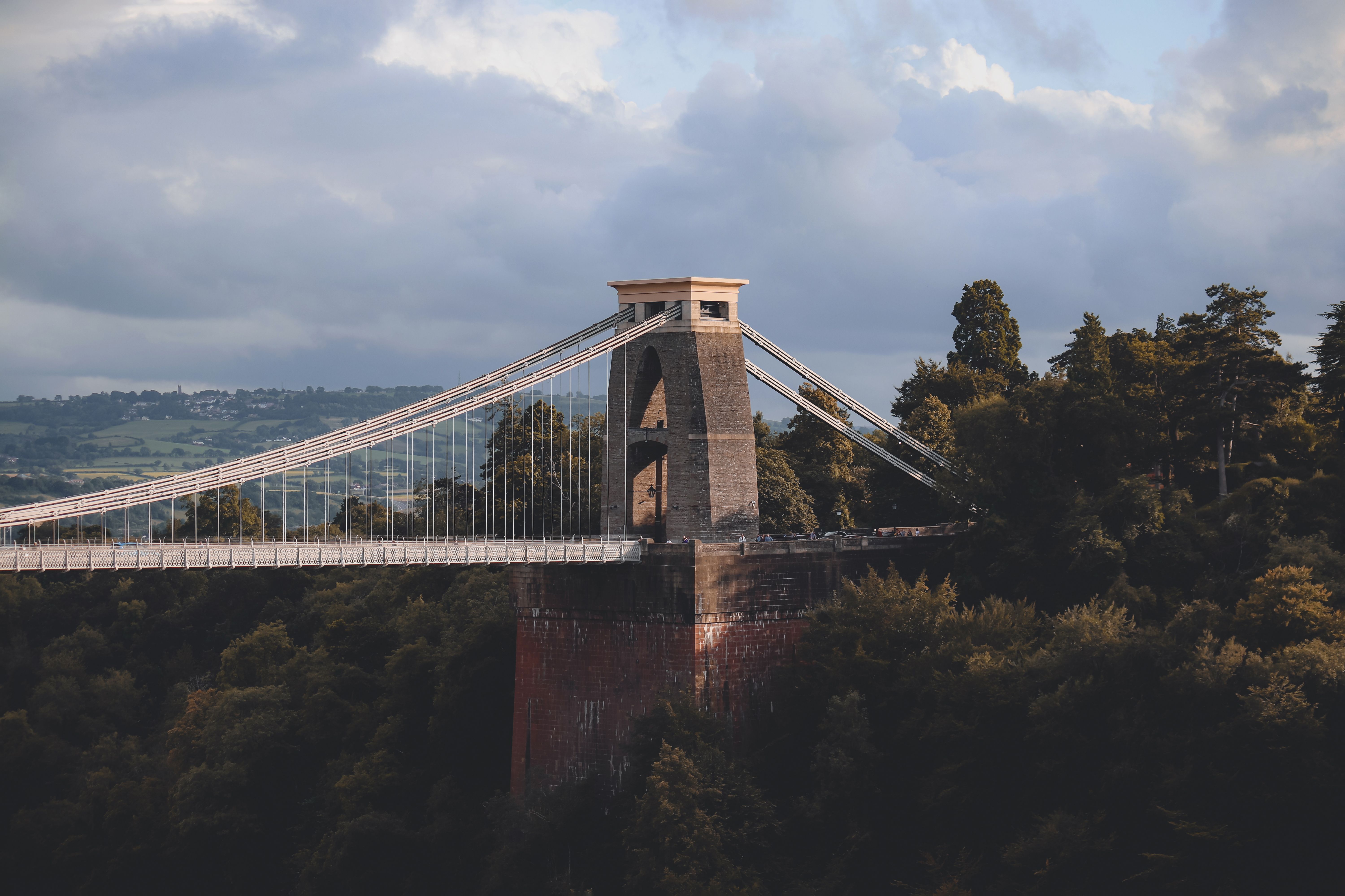 Scenic view of Clifton Suspension Bridge spanning a lush forested valley under a cloudy sky.