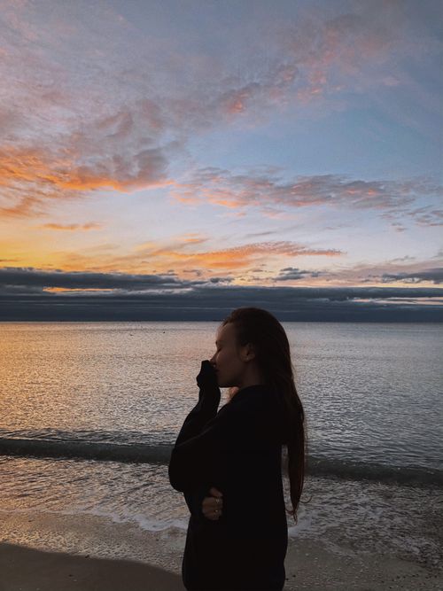 Free A woman in a jacket stands by Odessa's beach at sunset, creating a peaceful silhouette against the colorful sky. Stock Photo
