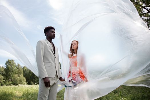 Stylish models posing with flowing fabric in a serene outdoor setting, showcasing modern fashion.