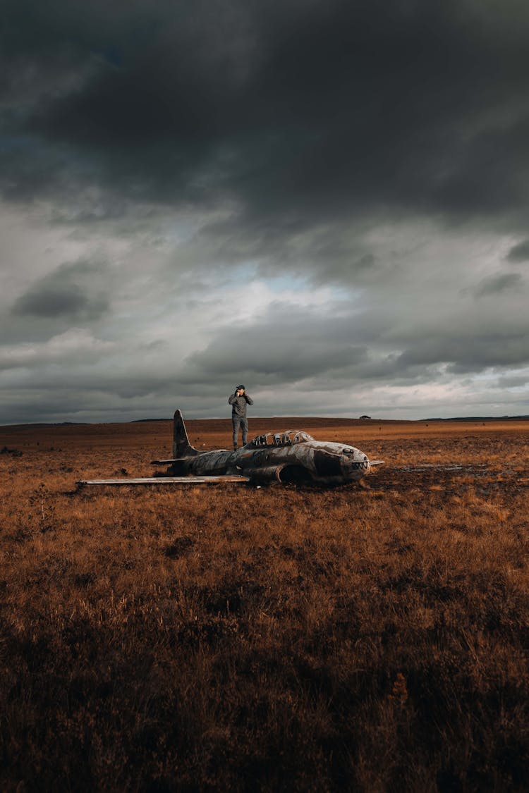 Pilot Standing On Small Airplane Fuselage Laying In Middle Of Autumn Fields