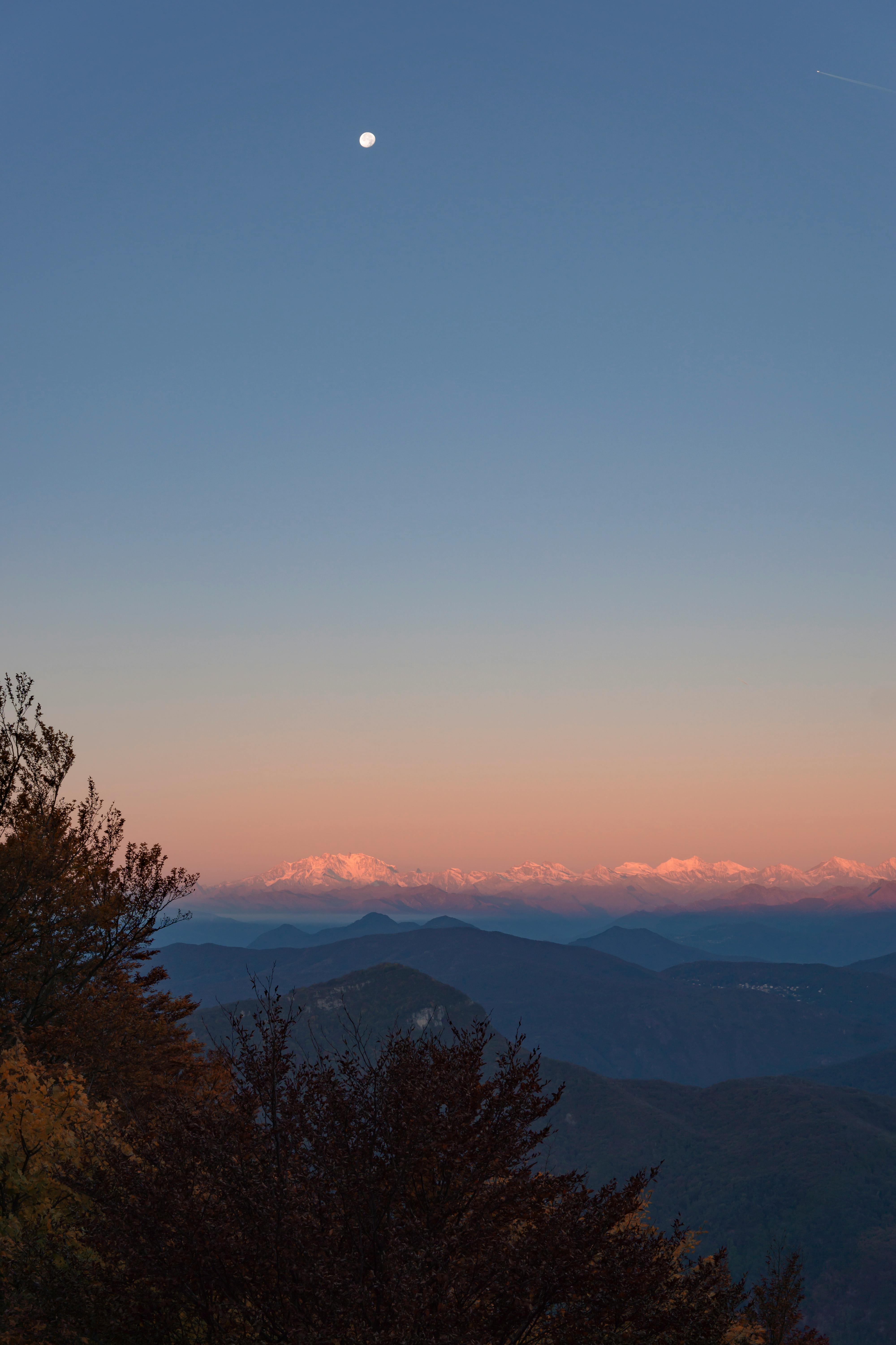 A stunning view of the Alps during sunset with a clear sky and visible moon in Switzerland.