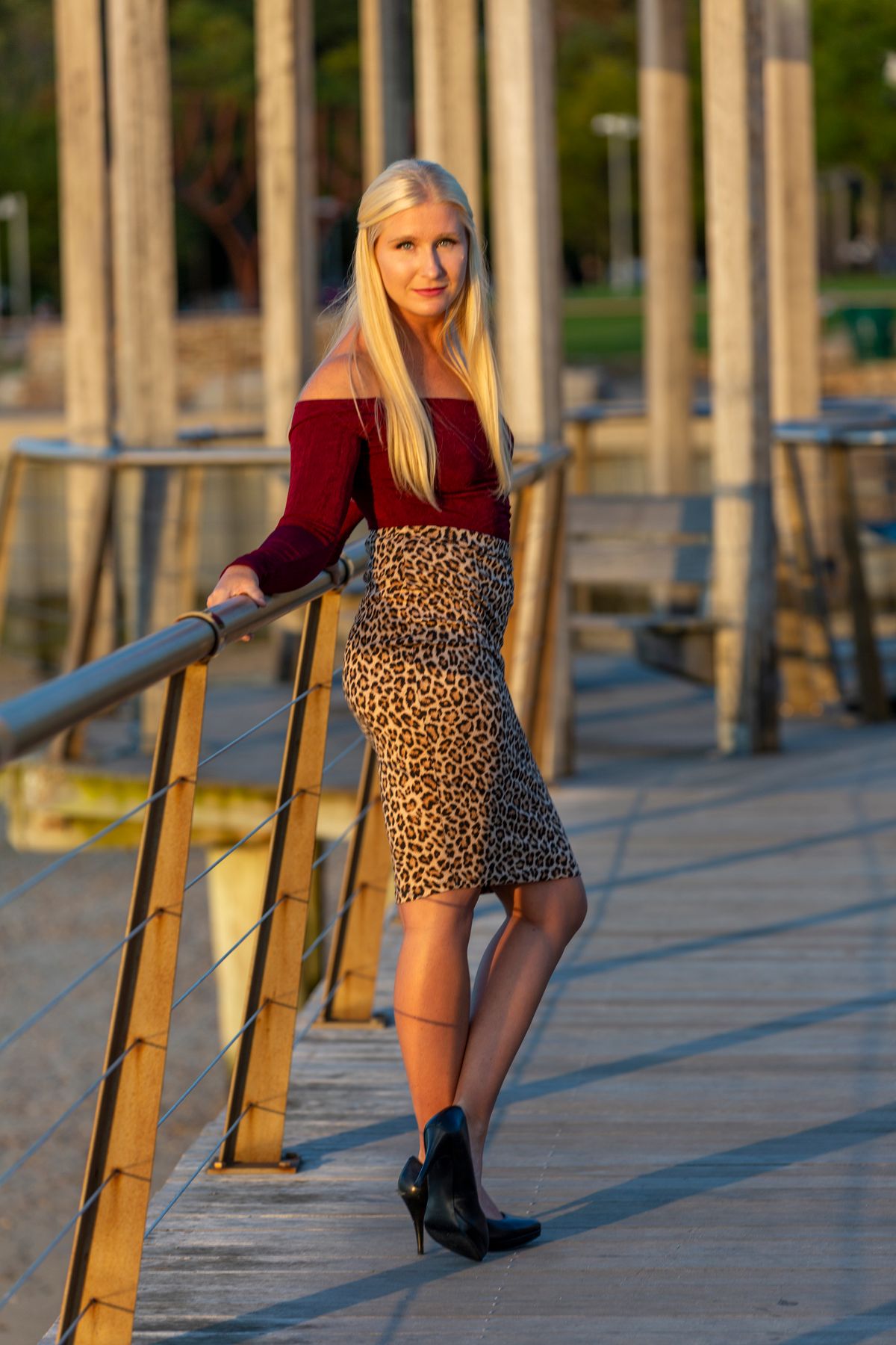 Woman pairing a leopard print midi pencil skirt with a burgundy off the shoulder top and black pumps at golden hour