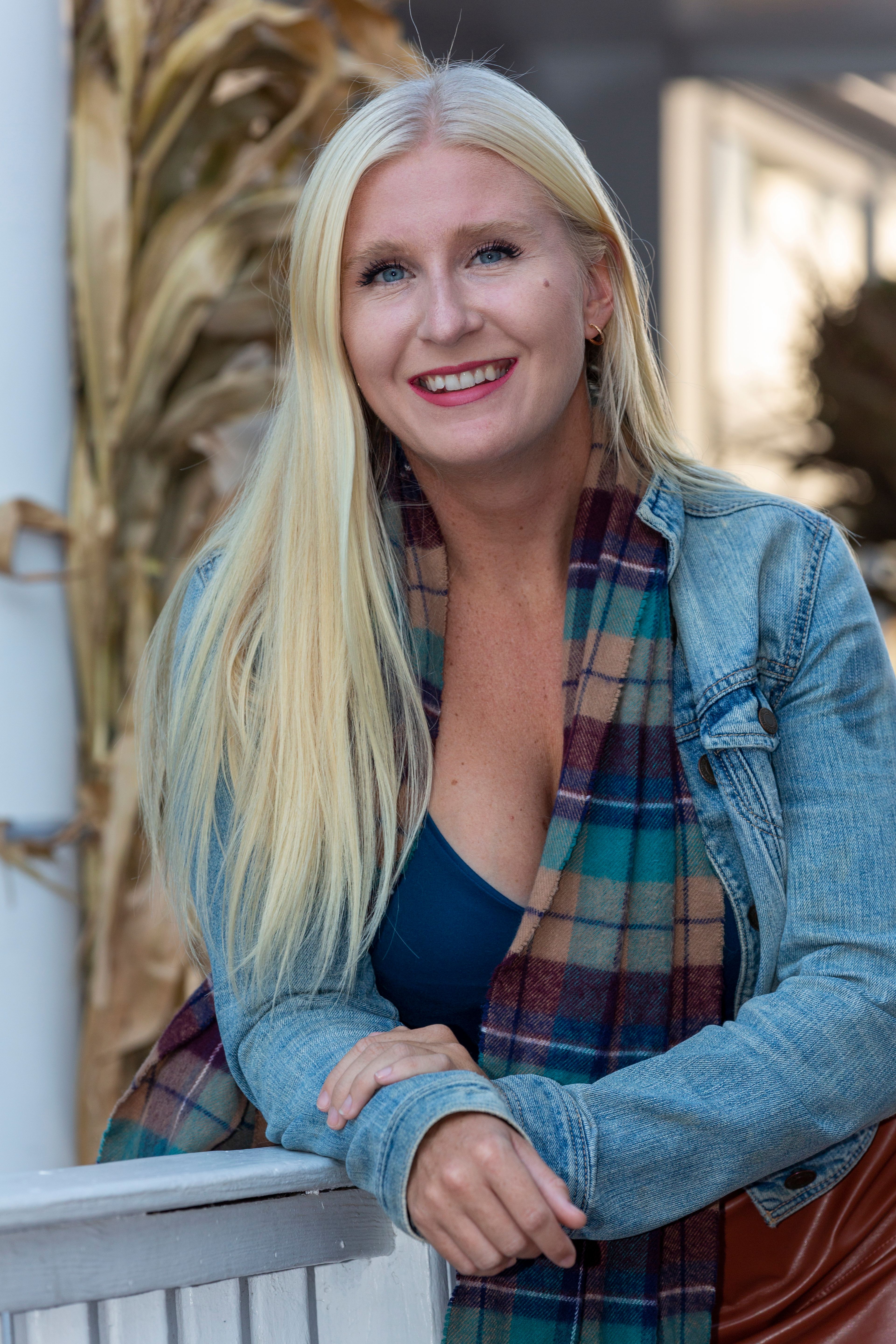 Smiling woman with long blond hair, wearing a denim jacket and scarf, posing outdoors.