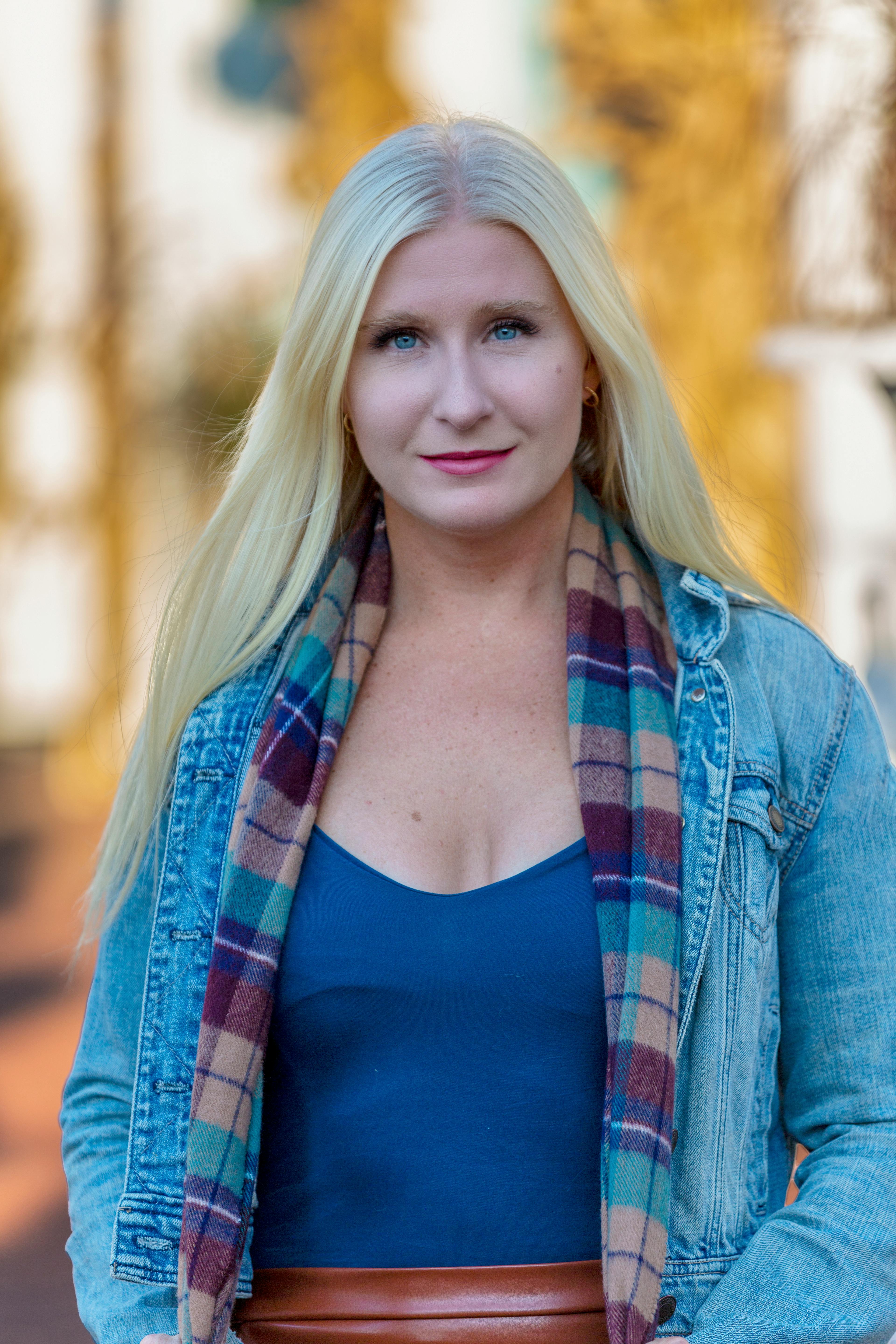 Stylish woman with long blond hair in denim jacket posing outdoors.
