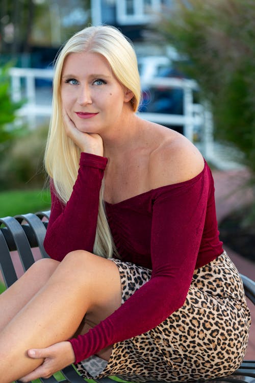 Free A Pretty Woman in Red Off-Shoulder Sleeves and Leopard Print Skirt Sitting Stock Photo