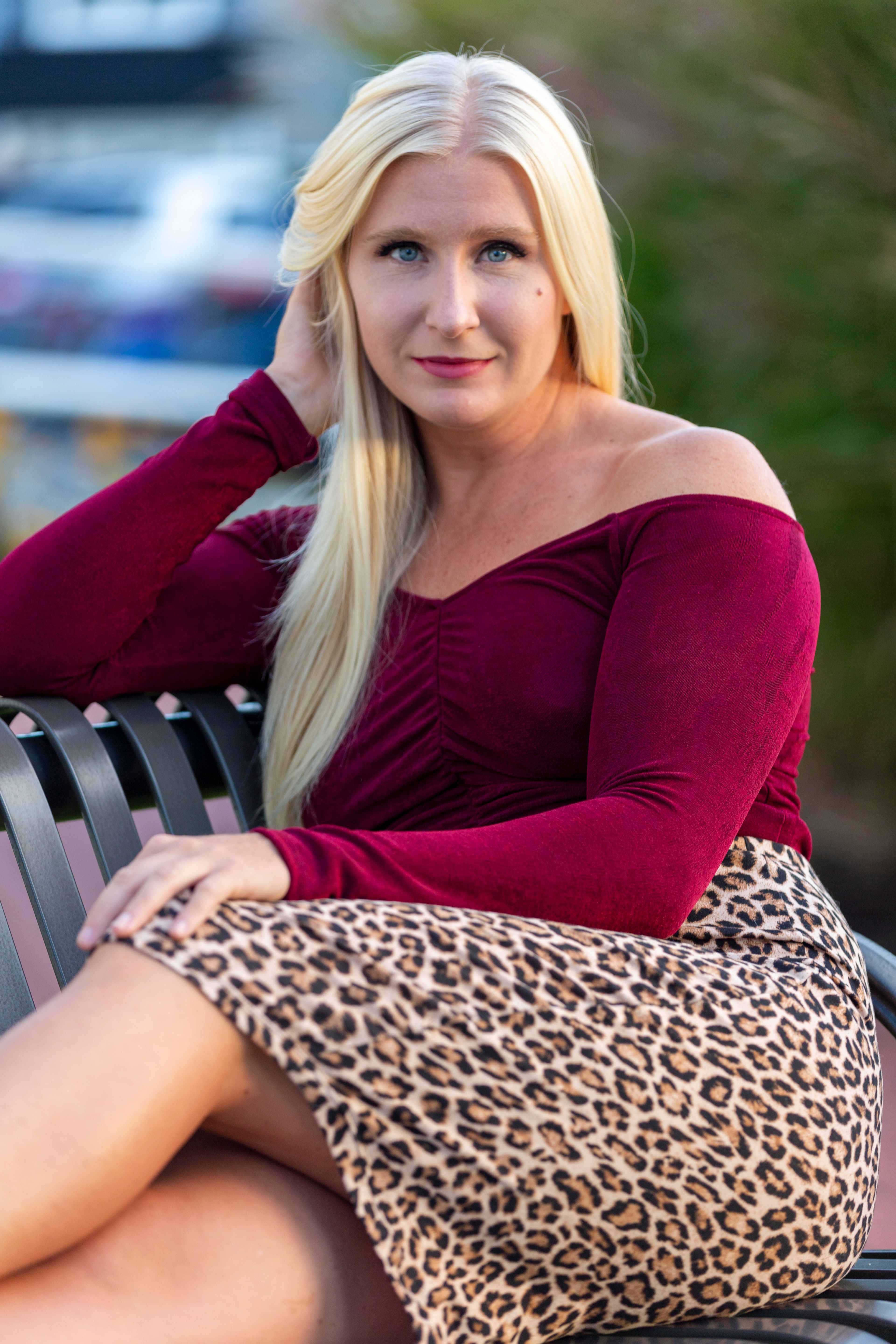 Elegant woman with blonde hair in a leopard print skirt sitting on a bench outdoors.