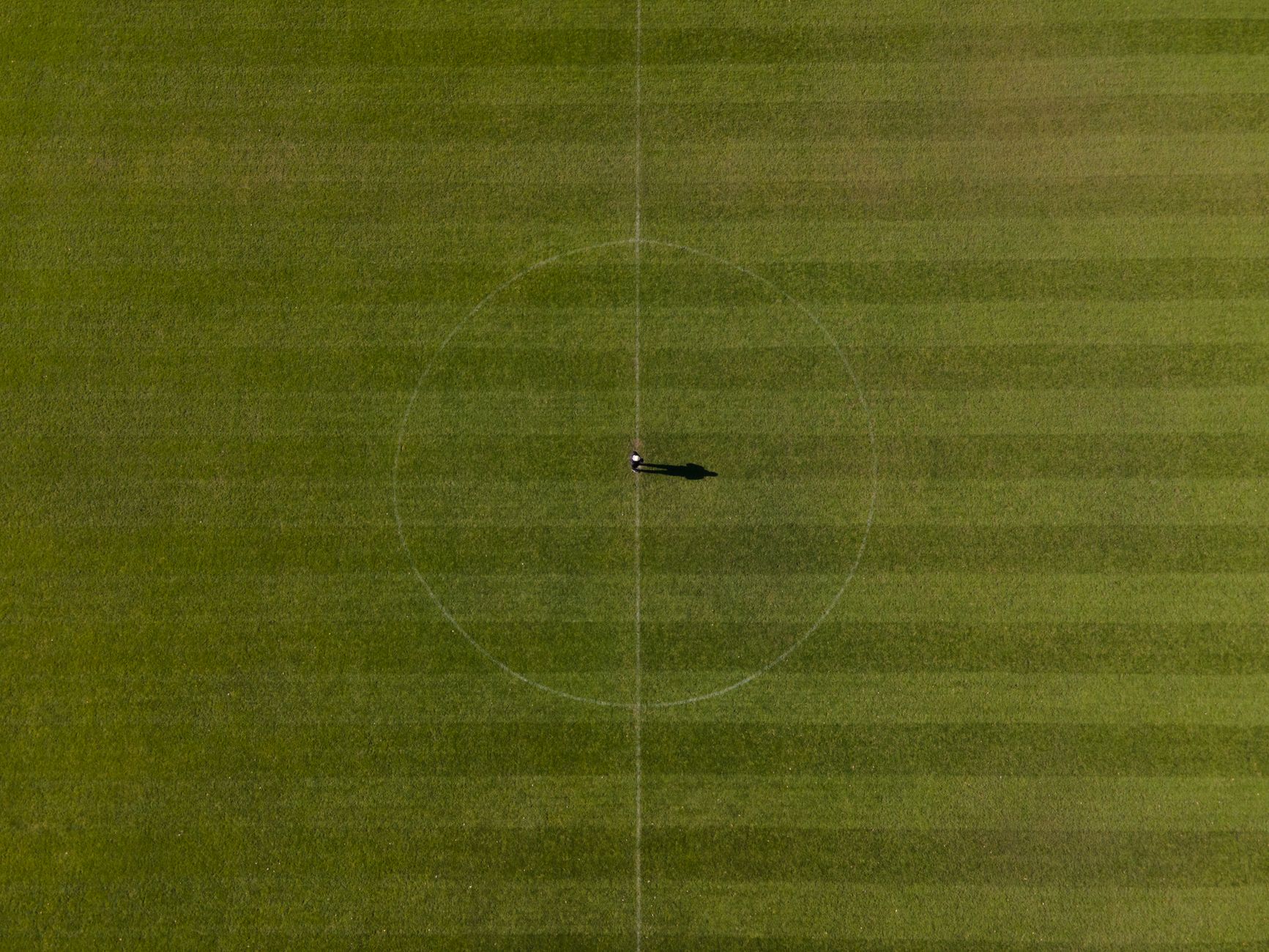 Drone shot of a soccer field with one person at the center circle, highlighting the vast green expan