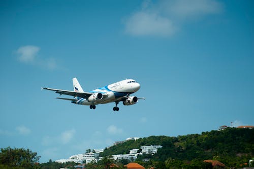 免费 白色和蓝色的客机经过绿树覆盖的山丘上 素材图片