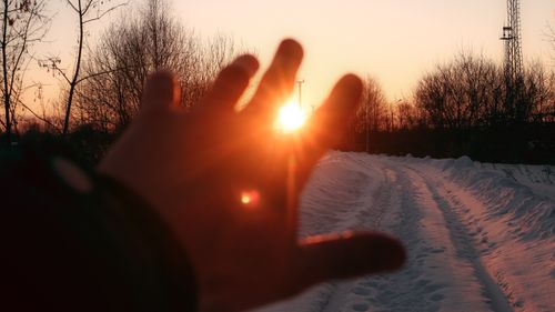 Free A hand reaching towards the setting sun on a snowy path, evoking warmth and tranquility. Stock Photo