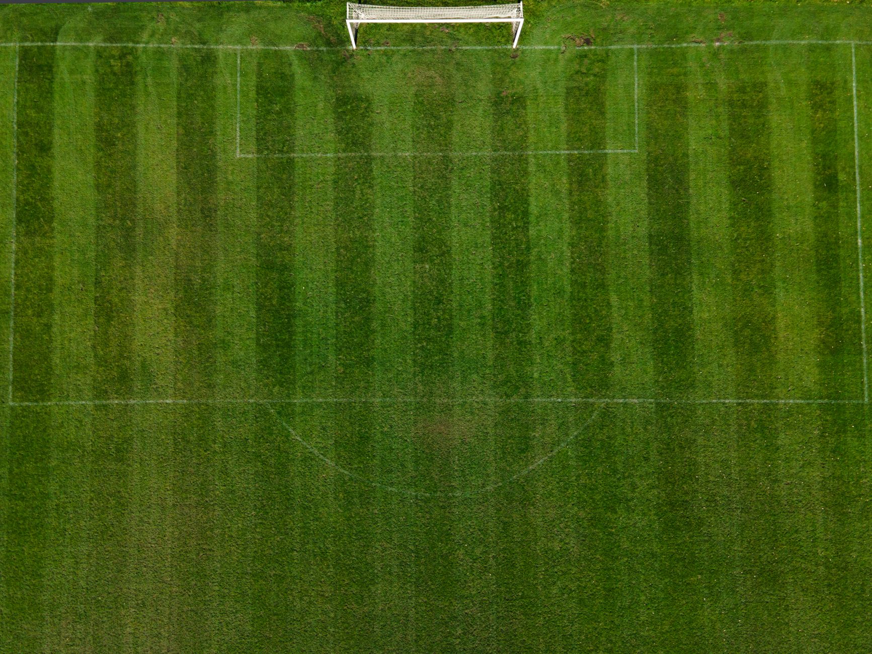 Drone shot capturing an aerial view of a well-maintained green soccer field with clear markings.