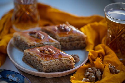Close-up of sweet baklava slices with walnuts on a plate, served with tea.