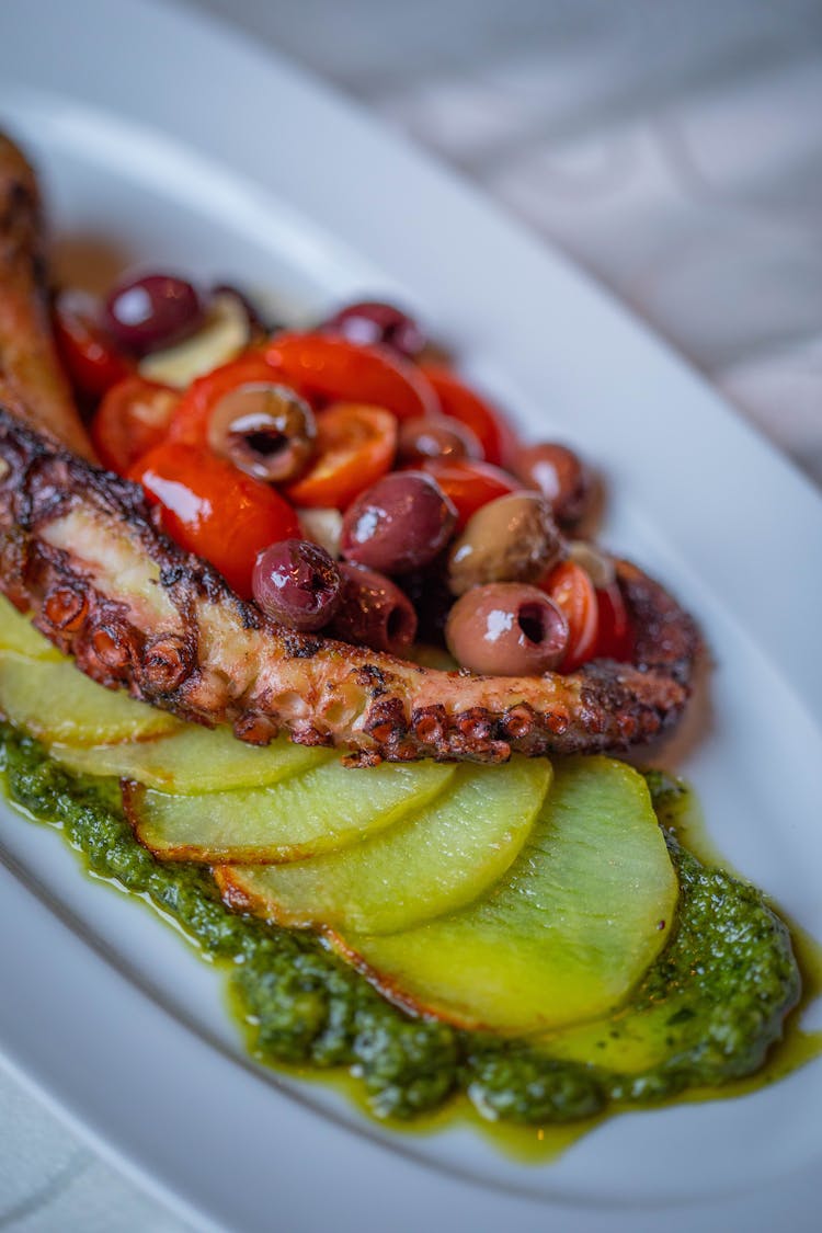 Appetizer Of Roast Octopus Olives Red Tomatoes Sliced Potatoes Served On Green Pesto