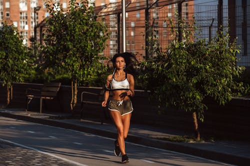 Free A Woman in White Tank Top Jogging on the Sidewalk Stock Photo