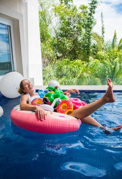 Woman enjoying pool relaxation with colorful float toys, surrounded by lush greenery.