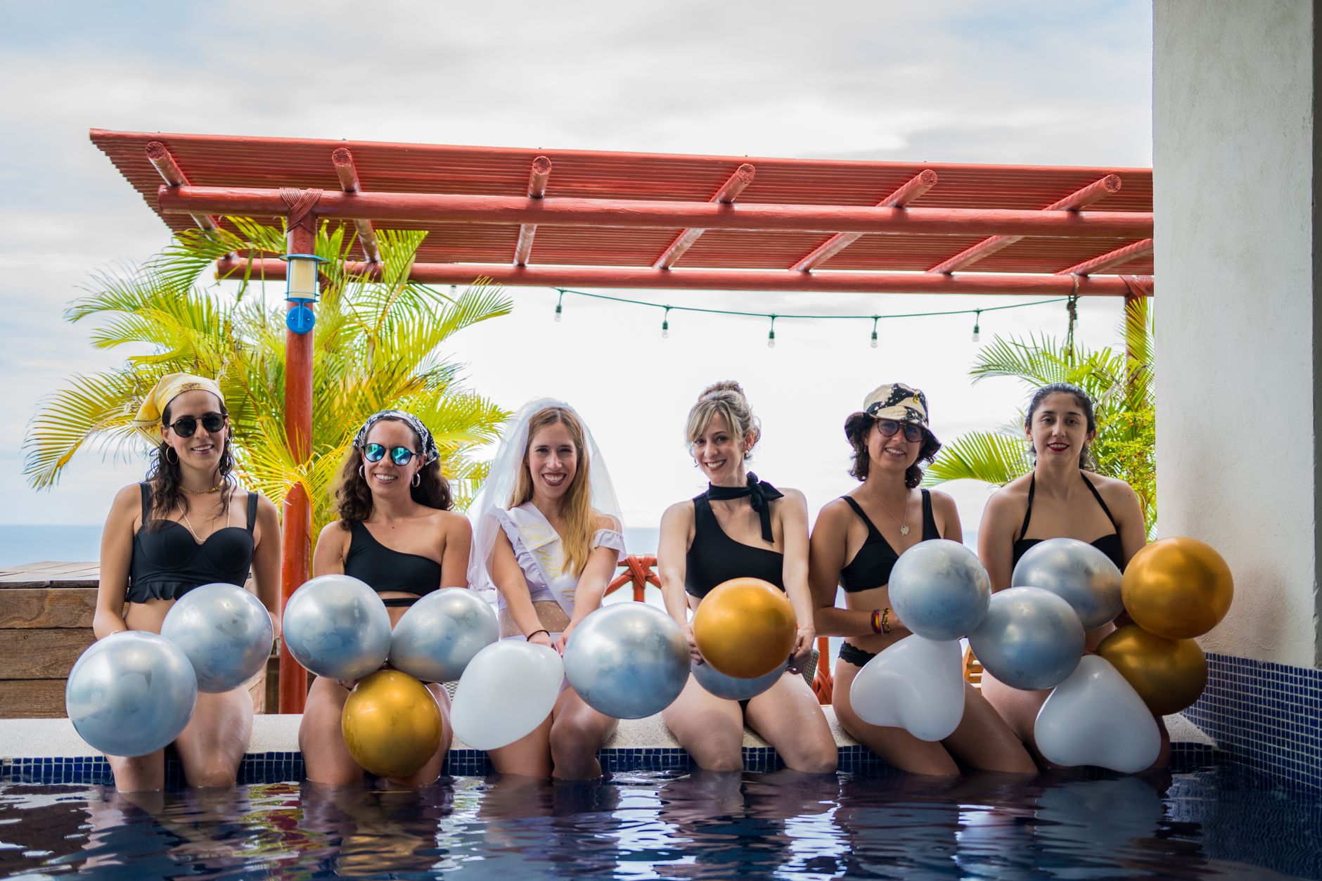 Group of women celebrating a bachelorette party outdoors with balloons by the pool.