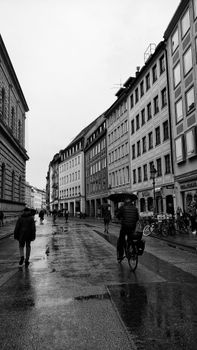 Black and white street view of Munich on a rainy day with cyclists and pedestrians.