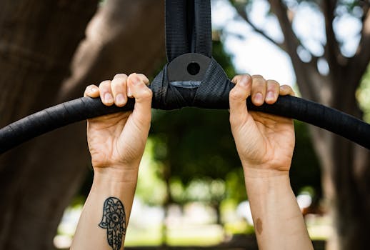Close-up of a person with tattoos holding fitness rings in an outdoor park setting.